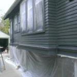 A house with painting in progress. The siding has been sprayed and areas are still masked.