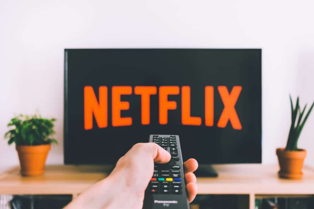 A hand pointing a TV remote at a TV with the Netflix logo across it