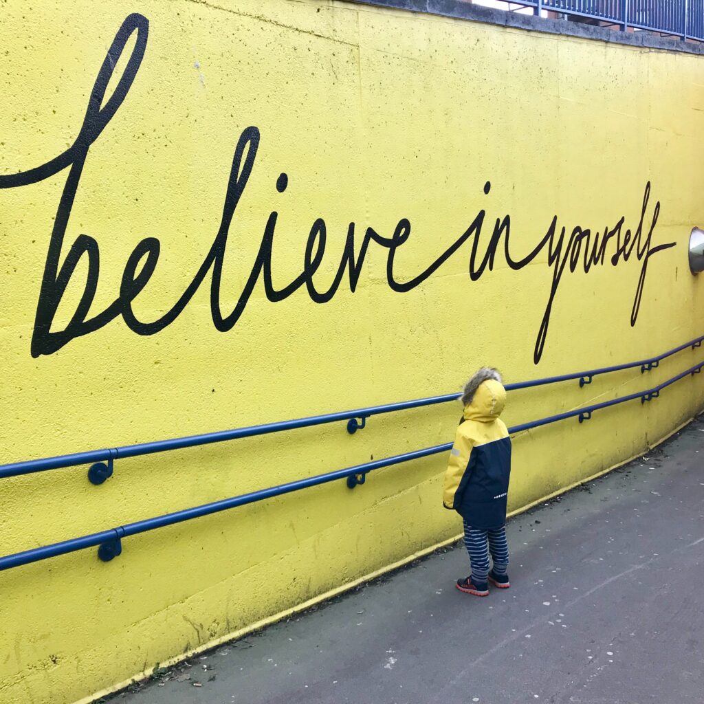 A child looking upon a mural that reads "believe in yourself" by Katrina Wright on Unsplash