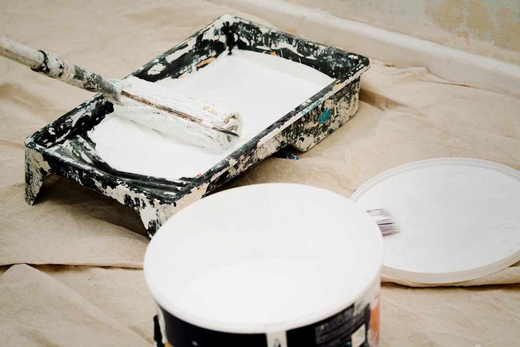 A paint roller in a pan with white paint